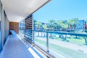 Een balkon met uitzicht op een zwembad, palmbomen en moderne gebouwen.
