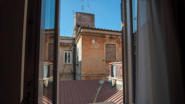 A view through a window of a building with a red roof, a chimney, and a balcony. - Apartment in Pigneto (Rome)