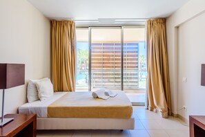 A hotel room with a bed, a desk, and a view through a sliding door to an outdoor area. - Vila das Lagoas Salgados Retreat (Albufeira)