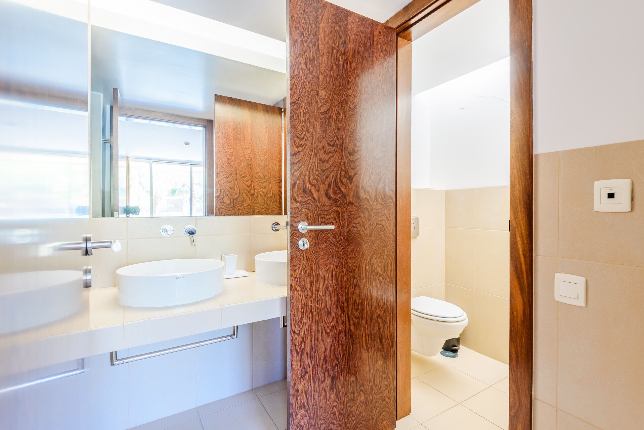 A modern bathroom with a wooden door, a white sink, and a toilet.