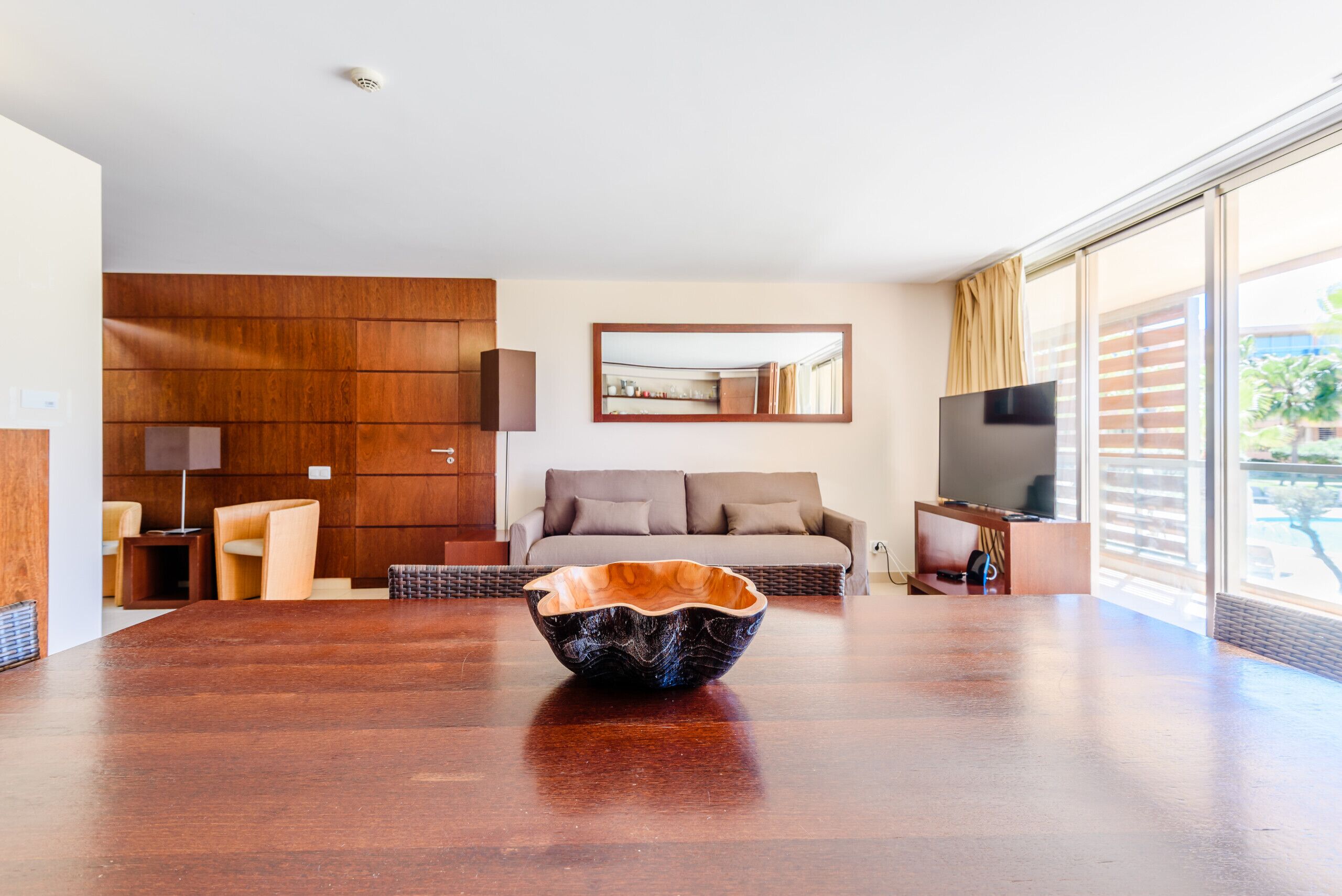 Una sala de estar moderna con una mesa de comedor de madera, un sofá, un televisor y un ventanal grande.