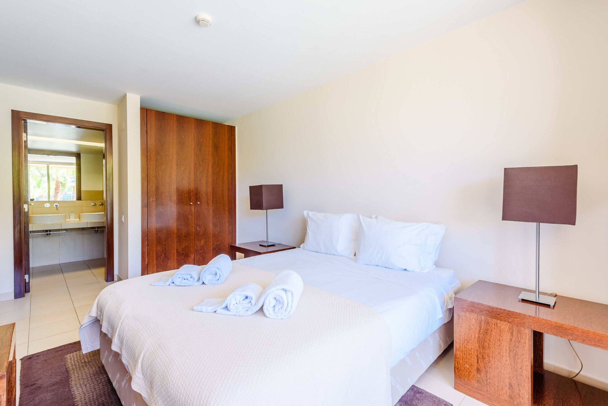 A hotel room with a large bed, wooden wardrobe, bedside tables, and a bathroom visible through an open door.