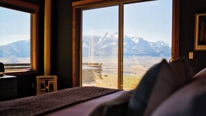 Ein Schlafzimmer mit großem Fenster und Blick auf die Berge, einem Kamin und einem Bett mit Kissen.