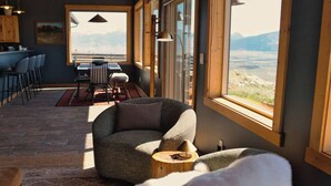 Ein modernes Interieur mit einer gebogenen Couch, einer Essecke und großen Fenstern, die einen Ausblick ins Freie bieten.