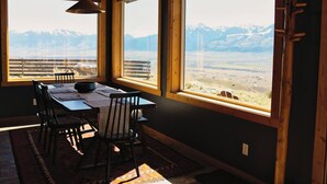 Ein Essbereich mit Tisch, Stühlen und Blick auf Berge durch große Fenster.