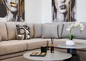 A modern living room with a sofa, a coffee table, a potted orchid, and a box of candles. - Aura Airport Suite (Spata)