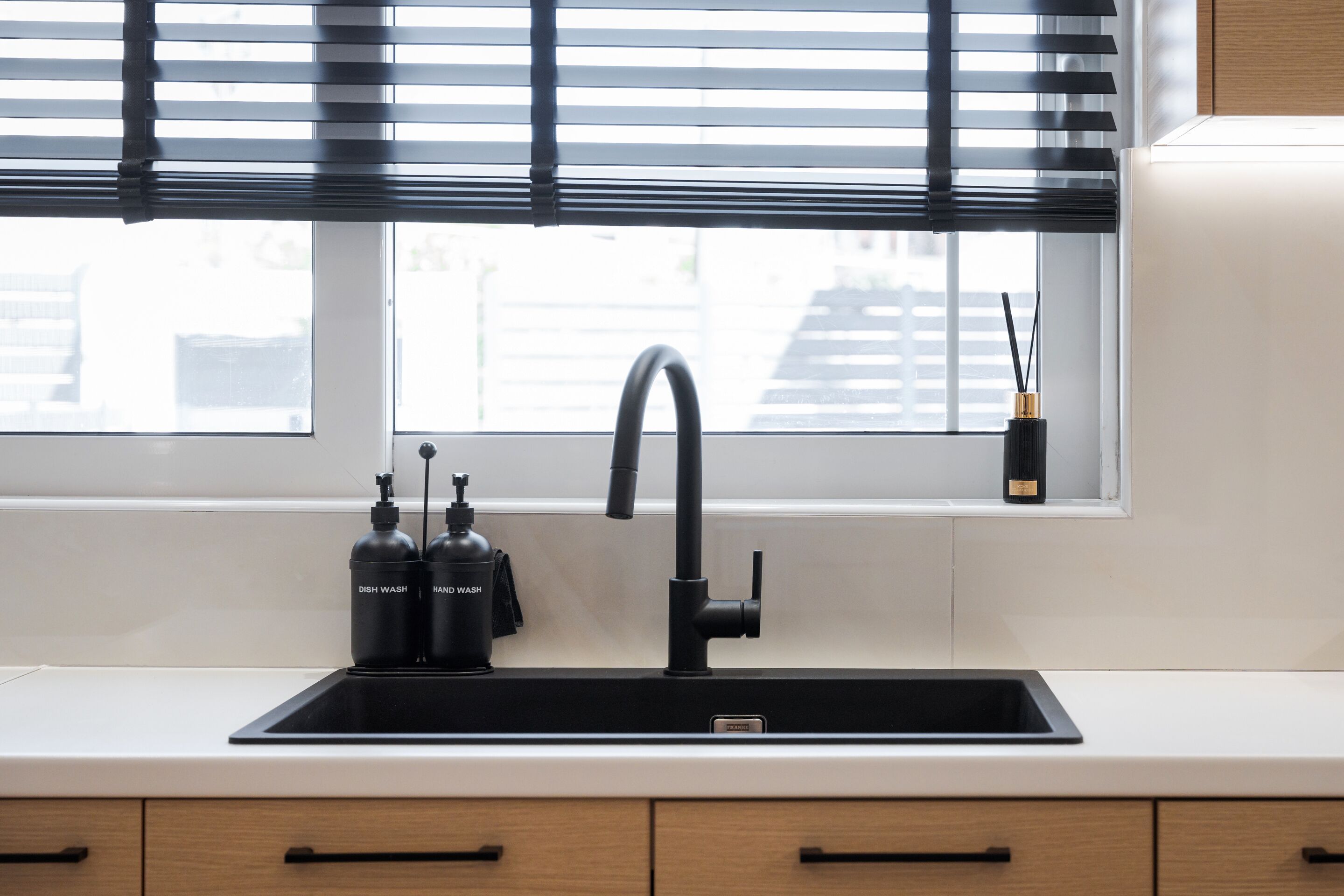 Una cocina moderna con un grifo negro, dos lavavajillas y un ventanal con persianas.