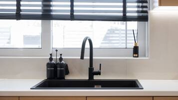 Una cocina moderna con un grifo negro, dos lavavajillas y un ventanal con persianas.