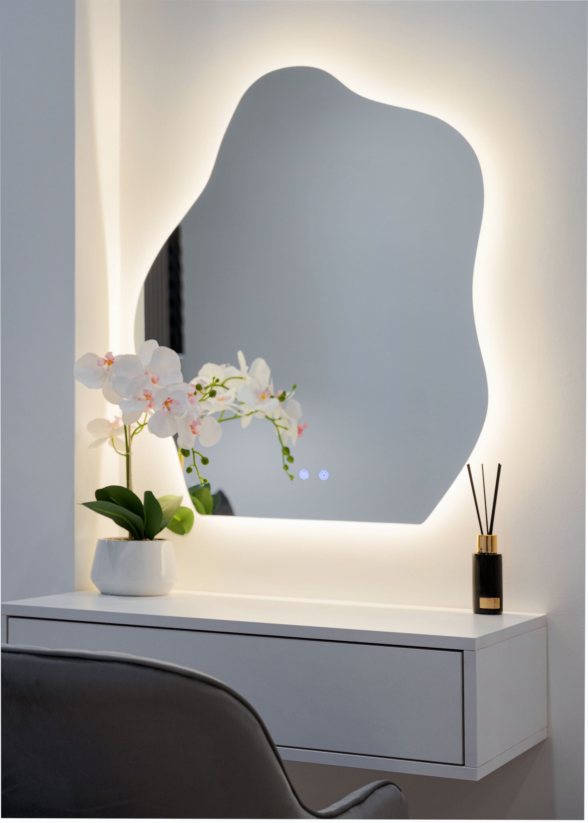 A white vanity with a large mirror, a potted orchid, and a reed diffuser.