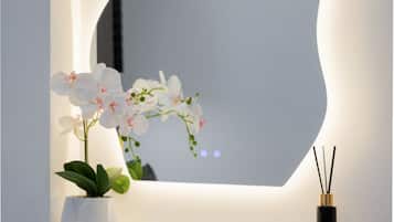A white vanity with a large mirror, a potted orchid, and a reed diffuser.