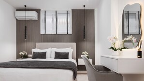 A modern bedroom with a bed, bedside table, chair, and a desk with a mirror. - Aura Airport Suite (Spata)