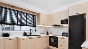 A modern kitchen with light wood cabinets, a black refrigerator, a microwave, and a dishwasher. - Aura Airport Suite (Spata)