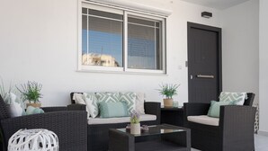 A modern outdoor seating area with wicker furniture, a glass coffee table, and potted plants. - Aura Airport Suite (Spata)