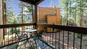 Eine Holzterrasse mit Tisch und Stühlen, mit Blick auf eine bewaldete Gegend und eine Holzhütte.
