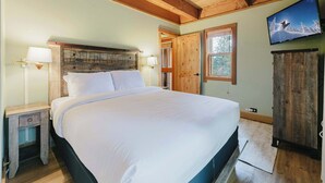 Ein Schlafzimmer mit Holzboden, einem Bett mit weißer Bettwäsche, einem an der Wand montierten Fernseher und einem Holzschrank.