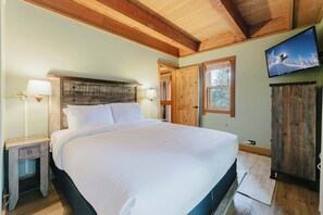 A bedroom with a wooden ceiling, a bed with white linens, a television on the wall, and a wooden wardrobe. - The Golden Bend Cozy Stay (Truckee)