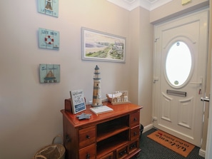 A room with a wooden dresser, a welcome sign, a framed landscape painting, and a door with a window. - The Willows (Romney Marsh)