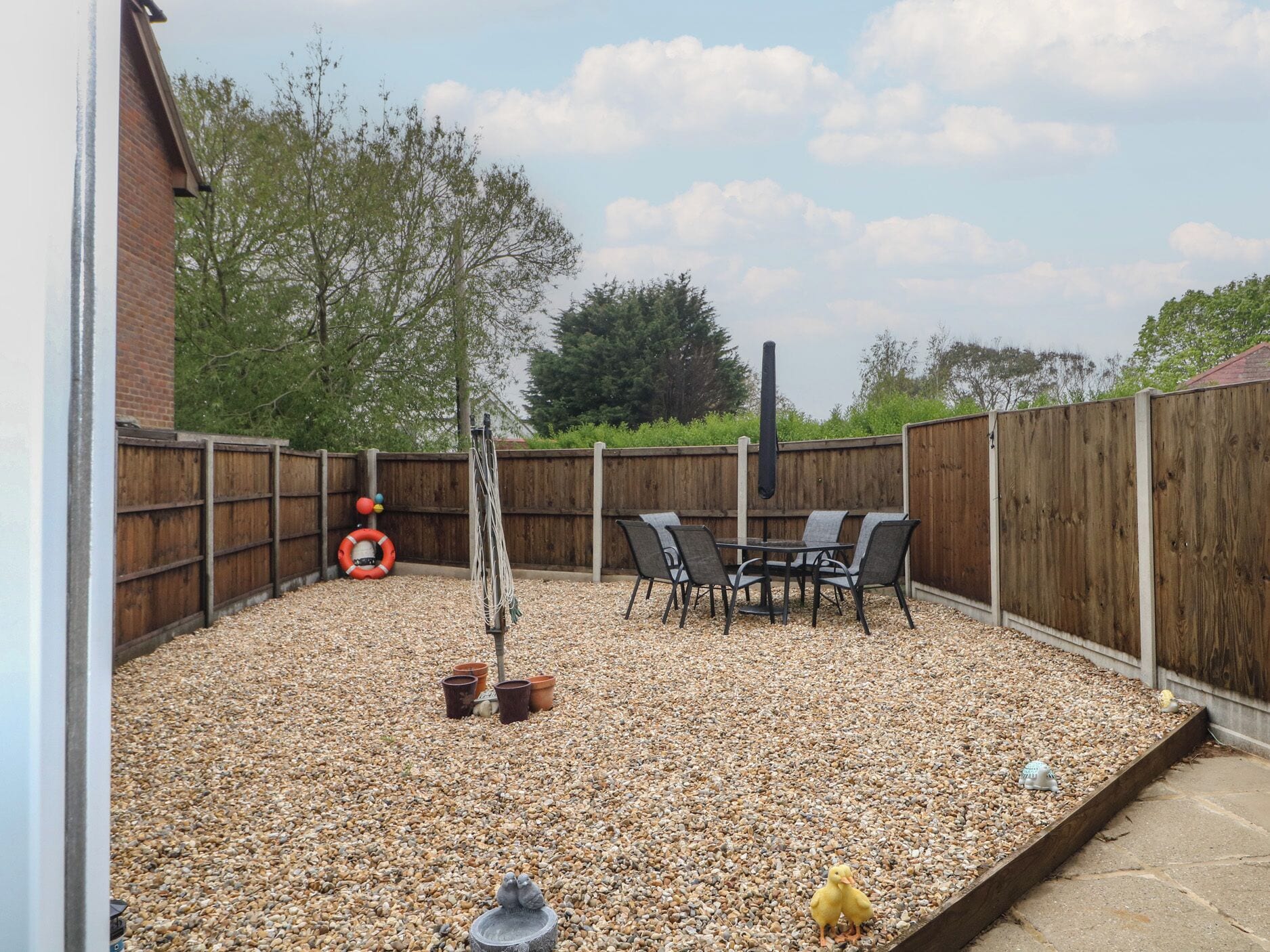 A patio with a table and chairs, surrounded by a wooden fence and pebbles.