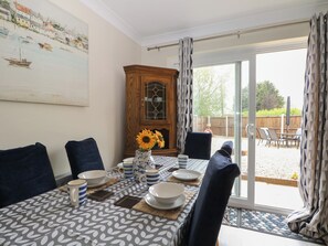 A dining area with a table set for four, a wooden cabinet, and a view of the backyard through a glass door. - The Willows (Romney Marsh)