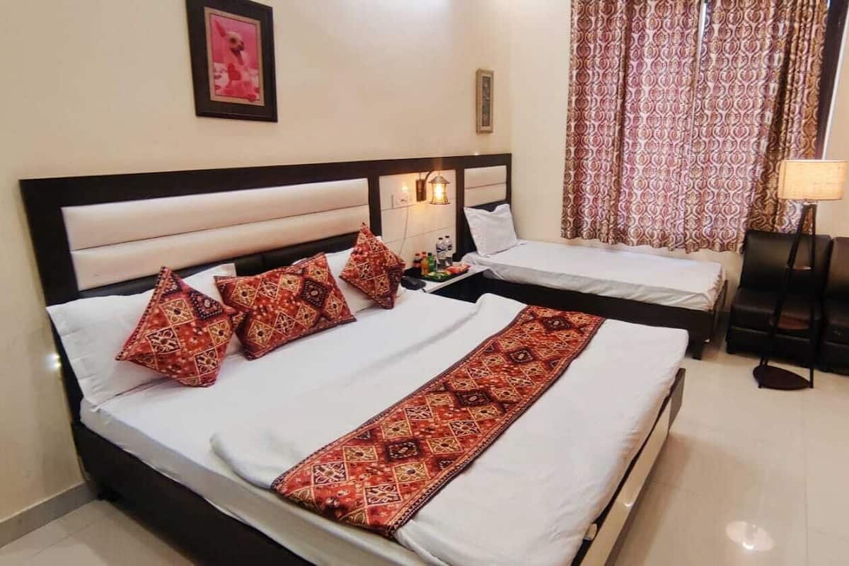 A hotel room with two beds, a nightstand, a lamp, and a patterned curtain.
