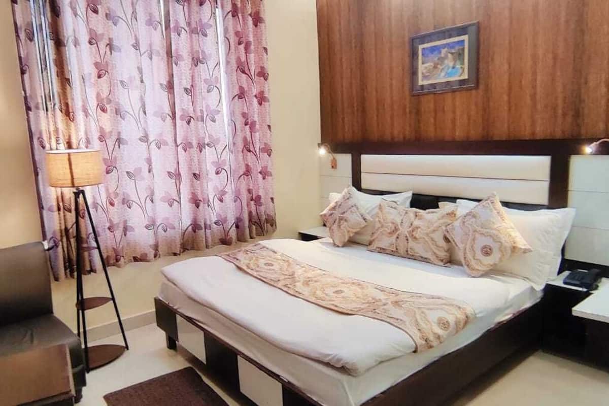 A hotel room with a bed, bedside table, lamp, and curtains.