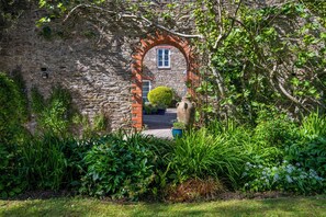 Ein Steinhaus mit einem Ziegelbogen, einem Fenster und einem kleinen Garten mit verschiedenen Pflanzen.