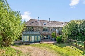 Ein Steinhaus mit Wintergarten, einem Ziegelweg und einem umzäunten Garten.