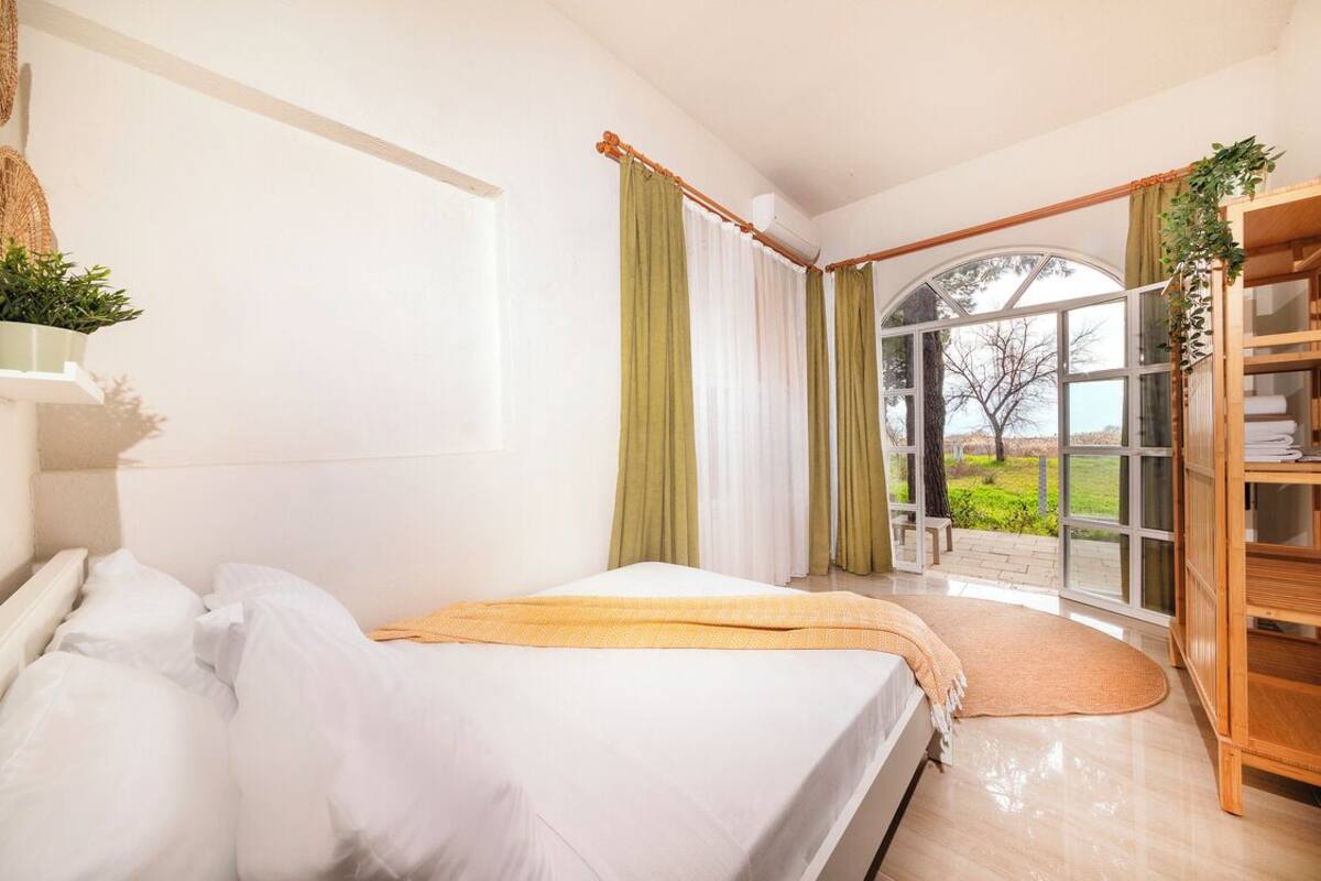 Une chambre à coucher avec un lit, une fenêtre avec des rideaux, une bibliothèque en bois et une vue sur l’extérieur.