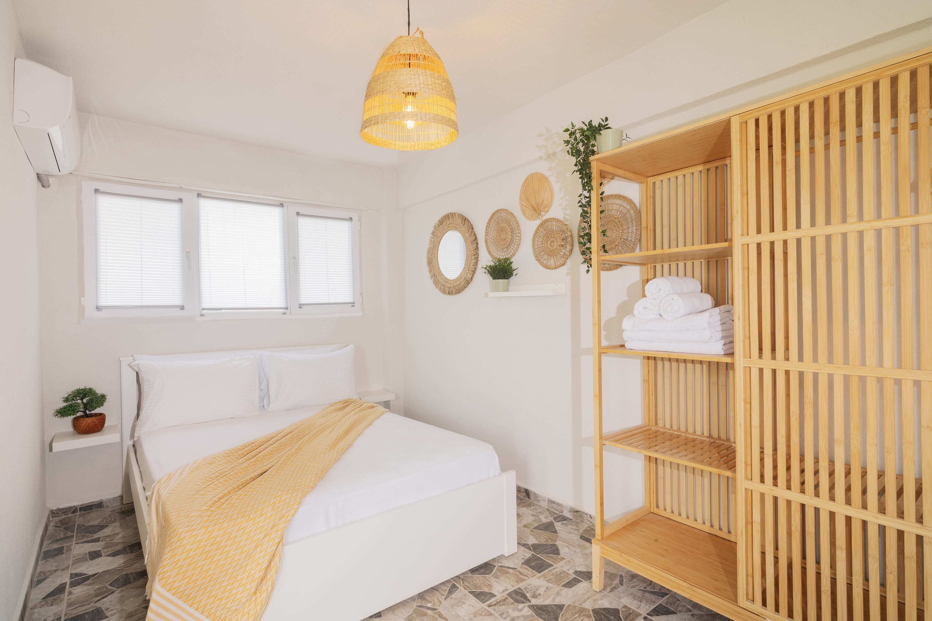 Un dormitorio con una cama, un armario de madera, una lámpara colgante y una ventana con persianas.