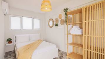 Un dormitorio con una cama, un armario de madera, una lámpara colgante y una ventana con persianas.