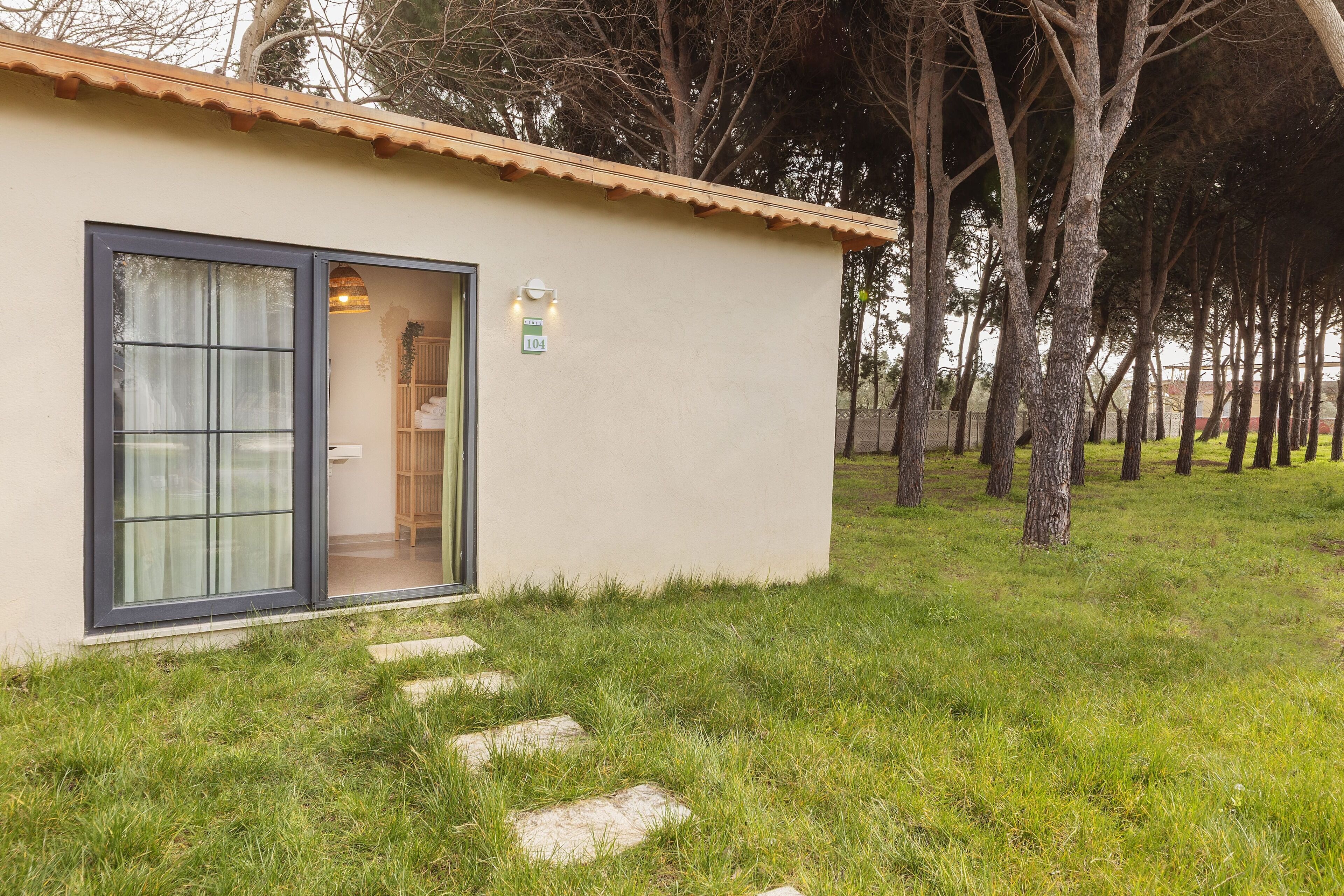 Un pequeño edificio con techo de tejas, puerta de cristal y un letrero con el número 104 en la pared.