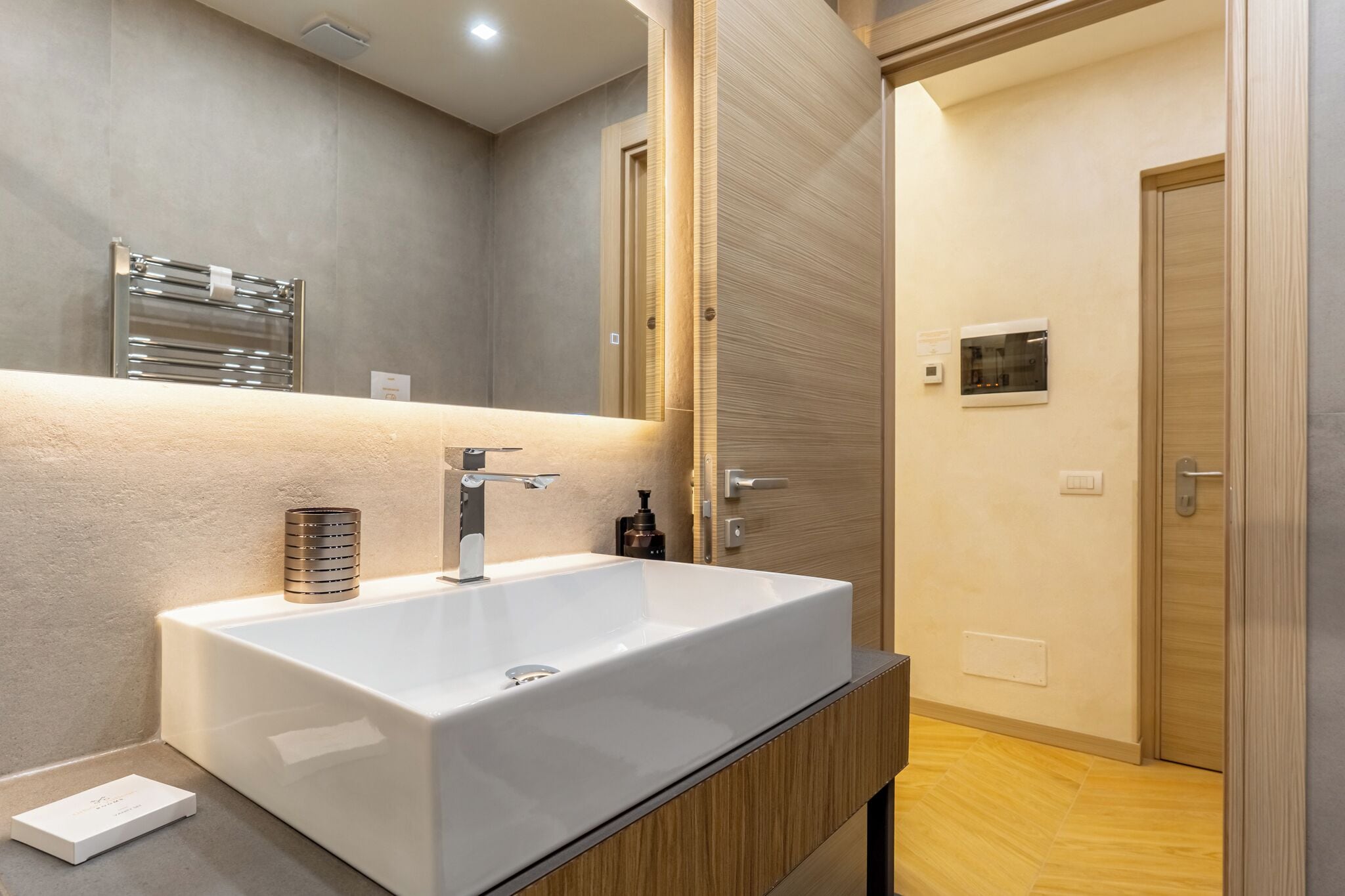 Un bagno moderno con uno specchio grande, un lavabo bianco e un mobile vanità in legno.