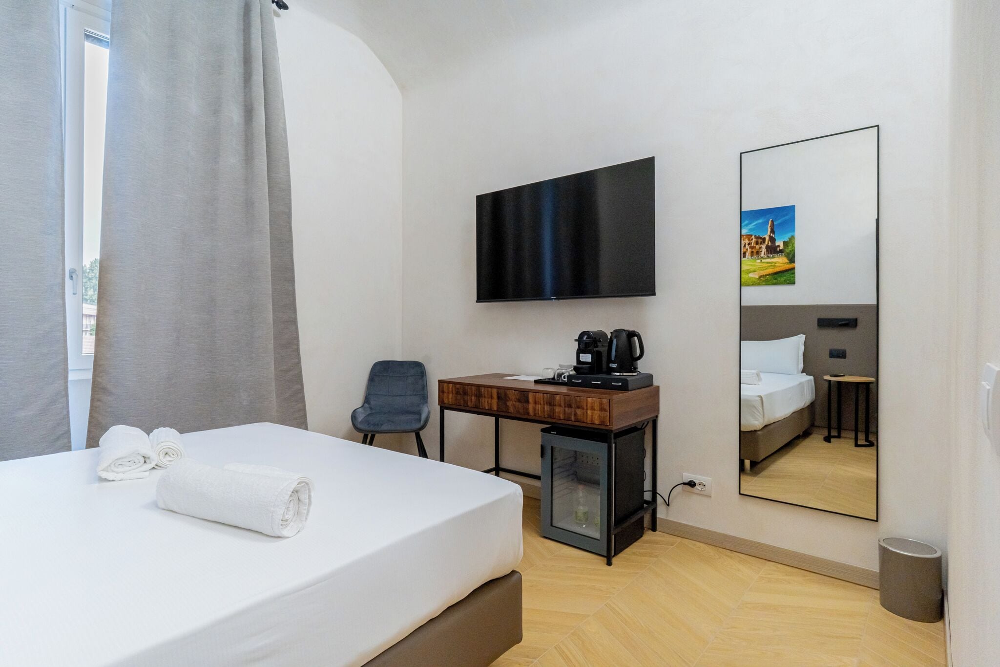 Habitación de hotel con cama, escritorio, televisión, cafetera y espejo.