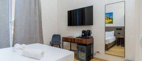Habitación de hotel con cama, escritorio, televisión, cafetera y espejo.