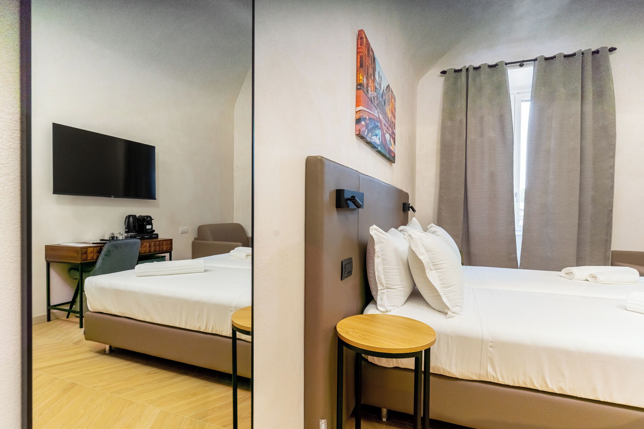 Ett hotellrum med en säng, ett skrivbord med en stol, en platt-TV som är monterad på väggen och en tavla ovanför sängen.