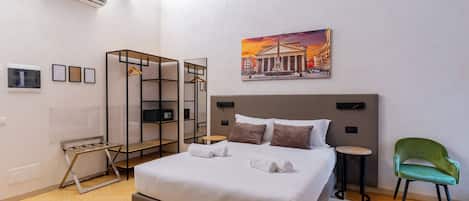 Un hotel moderno con una cama grande, una mesita redonda pequeña, una silla verde, un cuadro en la pared y un armario con espejo.
