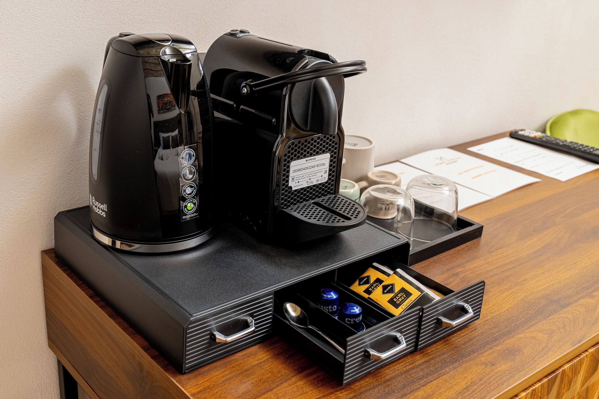 A coffee maker and a tea maker on a wooden table with a drawer containing coffee pods.