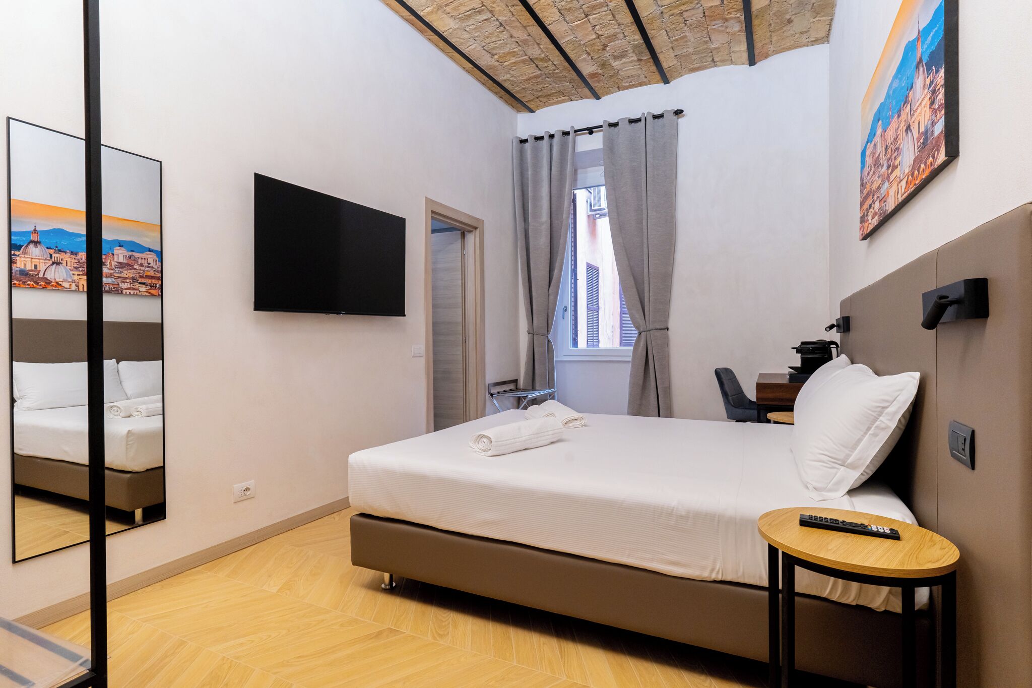 A hotel room with a bed, a TV, a desk, and a window with curtains.