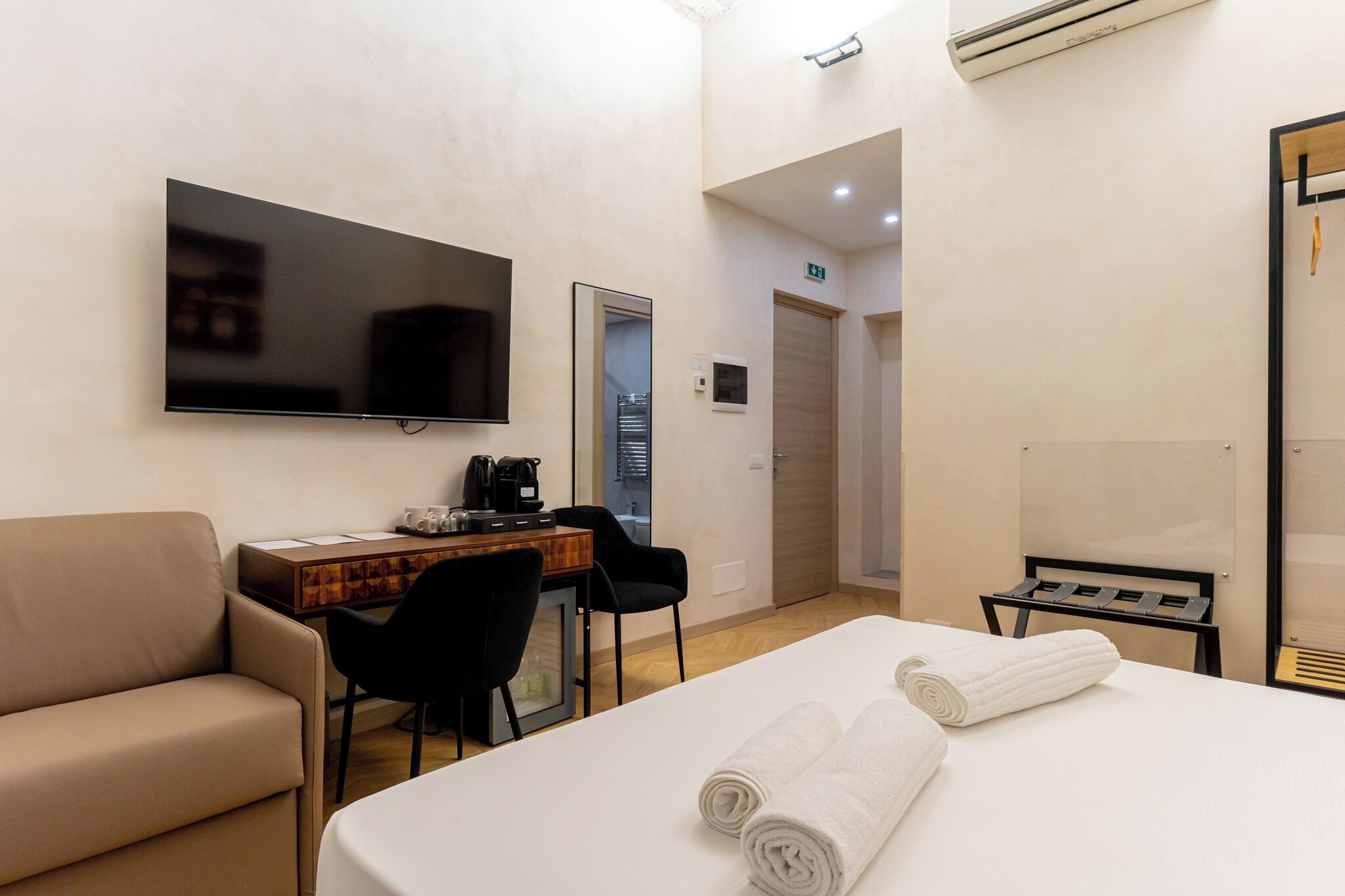 A hotel room with a bed, a desk, a TV, a sofa, and a bathroom door.