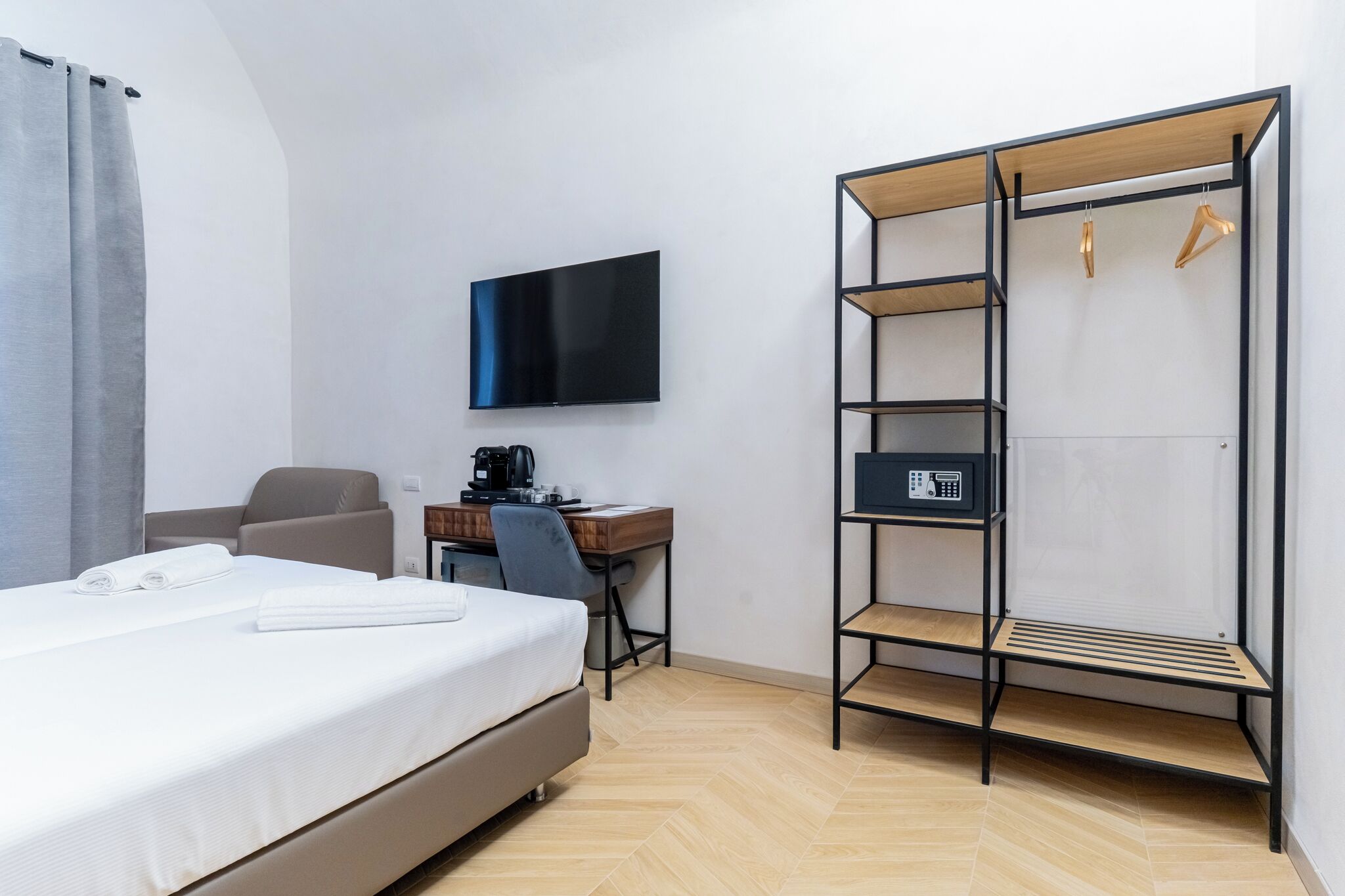 A hotel room with a bed, a desk with a chair, a TV, a wardrobe, and a heater.