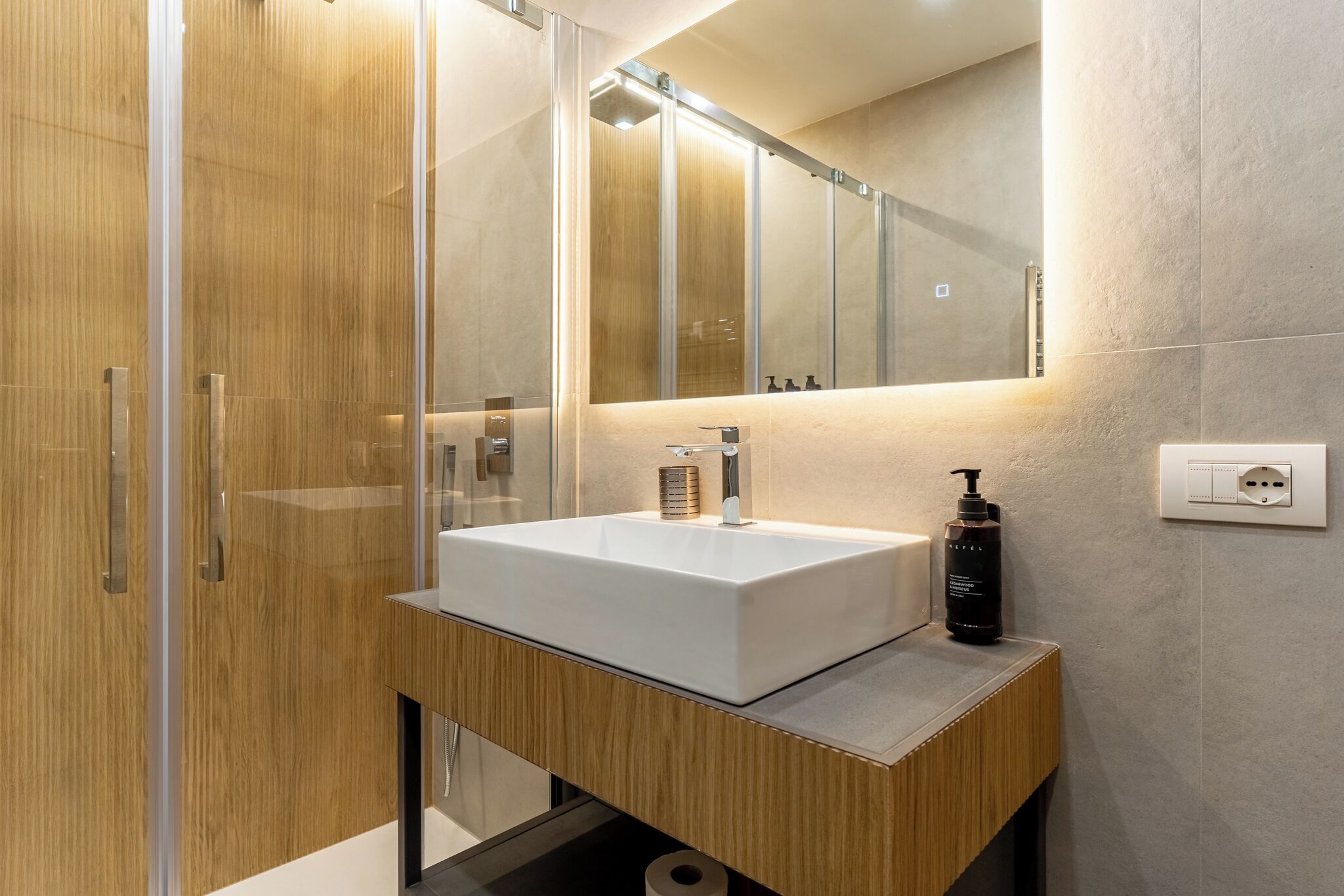 A modern bathroom with a large mirror, a white sink, and a wooden vanity.
