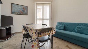 A living room with a teal sofa, a dining table with chairs, a flat-screen TV, and a painting of a sailboat. - Cozy 57m2 apartment, ideal for 3 people, located on the fifth floor of a building with lift.The property is located in the Navigli area, one of the areas most loved by citizens and tourists, in a context full of services. The location is also ideal for r (Milan)