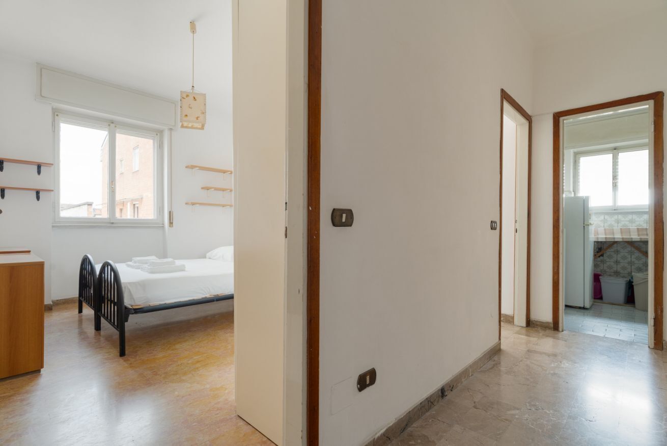 Une chambre à coucher comprenant un lit, une commode en bois, une fenêtre et une porte donnant sur une autre pièce.