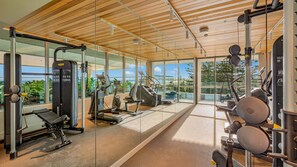 Ein Fitnessstudio mit unterschiedlicher Trainingsausstattung, großen Fenstern und einer Holzbalkendecke.