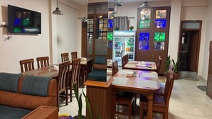 Un comedor con mesas y sillas de madera, un televisor montado en la pared y un refrigerador con luces de colores.