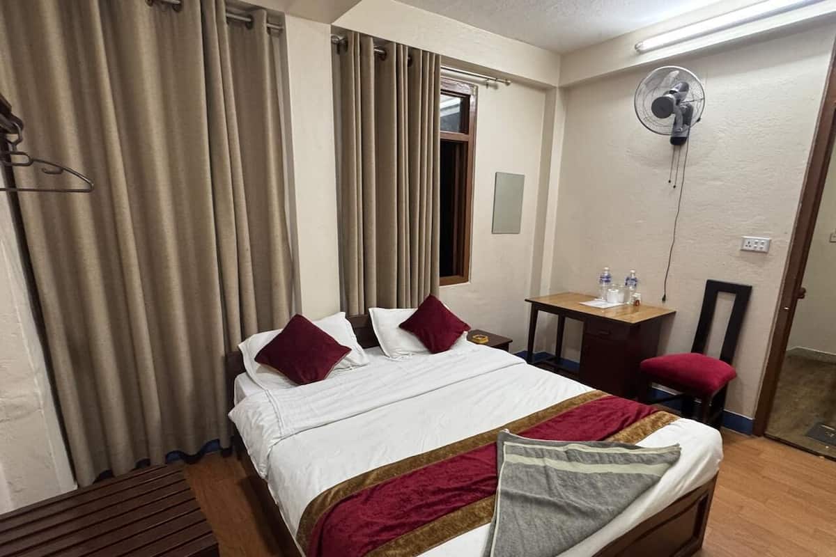 A hotel room with a bed, a desk, a chair, a fan, and curtains.