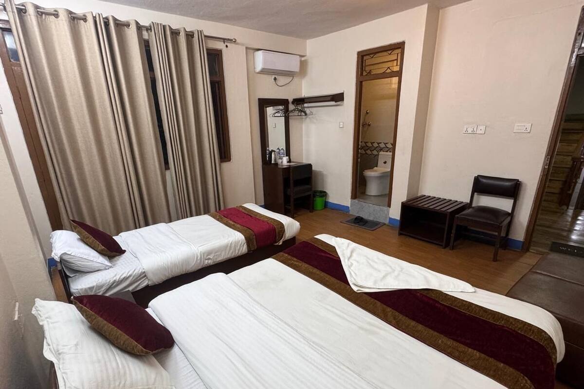 A hotel room with two beds, a small table, a chair, a mirror, and a shower area.