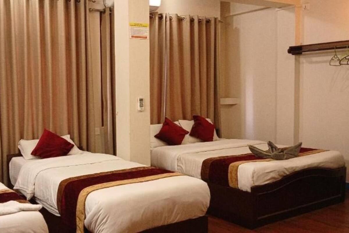 A hotel room with three single beds, each with a red pillow and a white blanket.