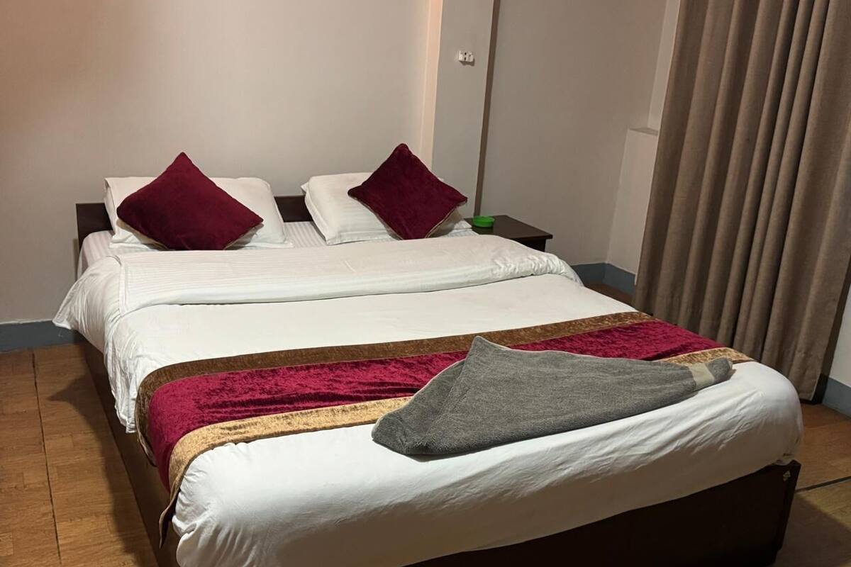 A double bed with white bedding, a red throw blanket, and a grey pillow.