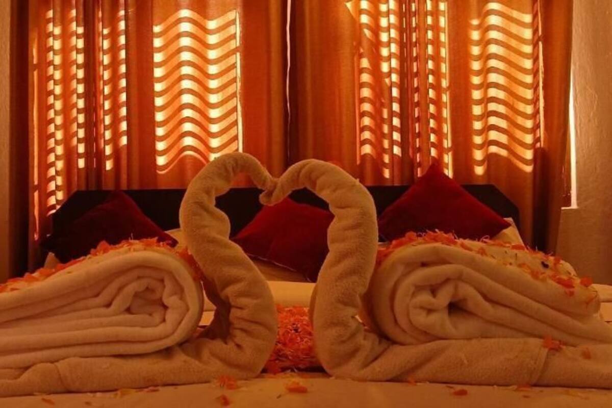A bed with towels arranged in the shape of swans, a red pillow, and a bedspread with flower petals.